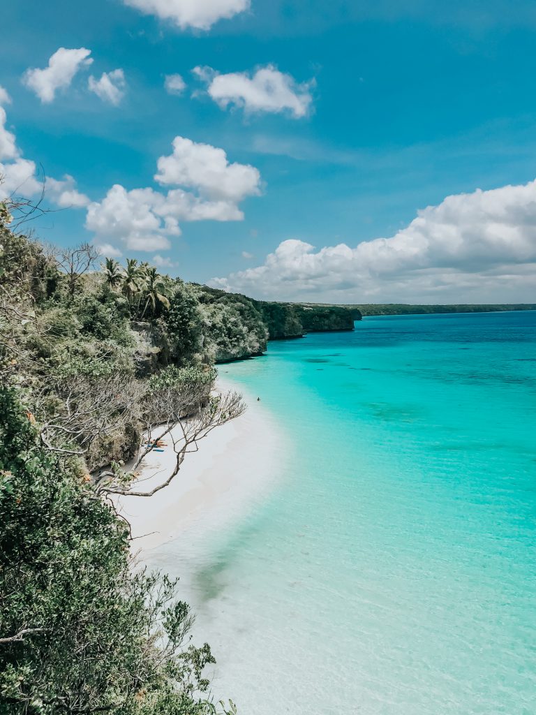Vu à l'arrivée du chemin, vu sur la mer bleue et un banc de sable blanc au pied des falaises, kiki beach lifou